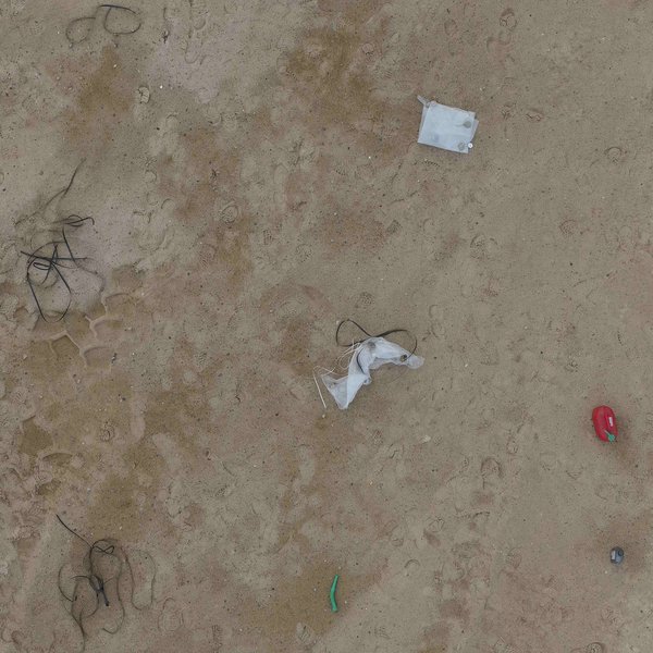 Drone image of a sandy test site on which various beach waste objects such as plastic tarpaulins, buoys and canisters are distributed.