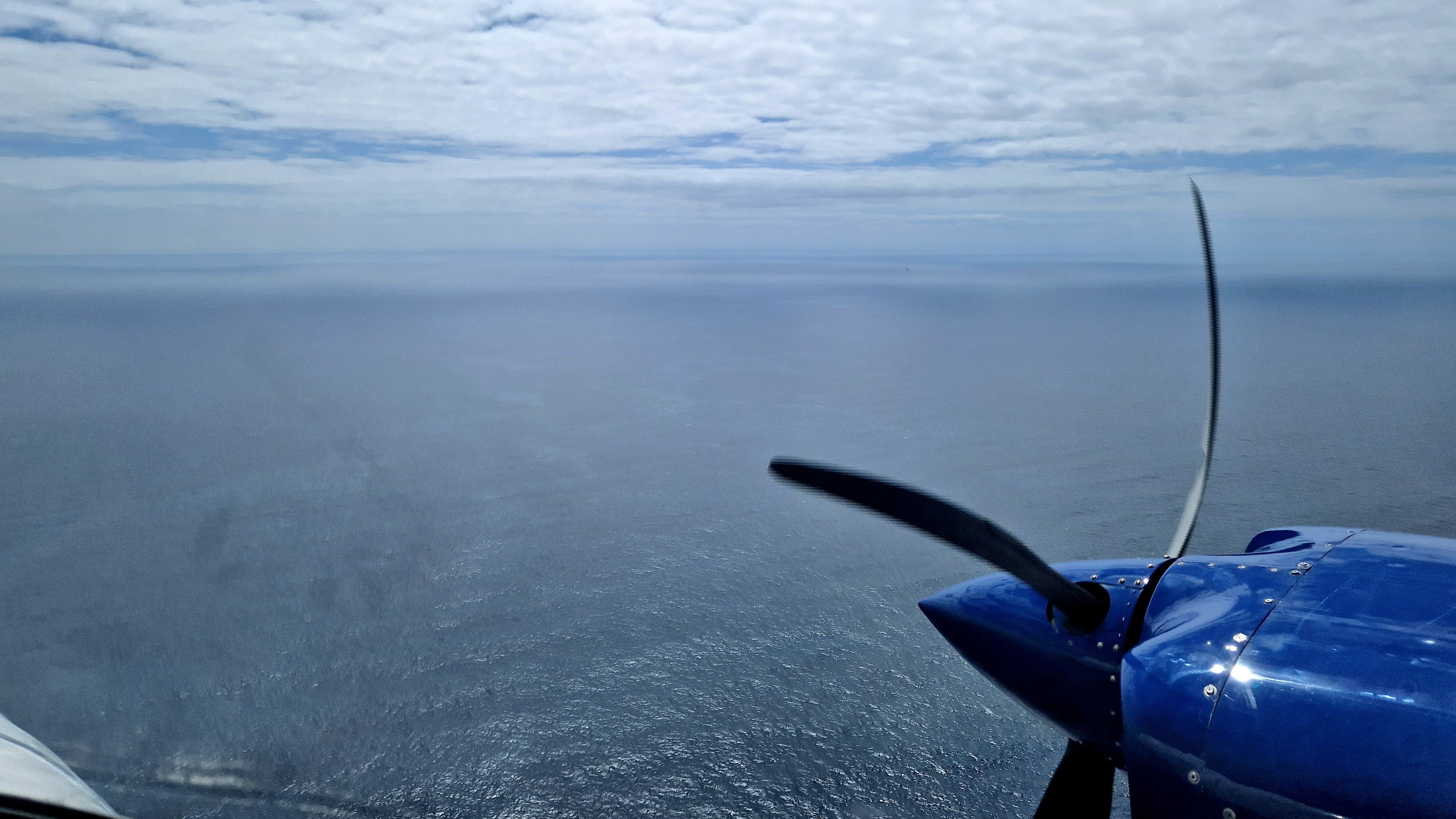 View of the sea from an aeroplane window, with the propeller of the aircraft in the front right of the image.