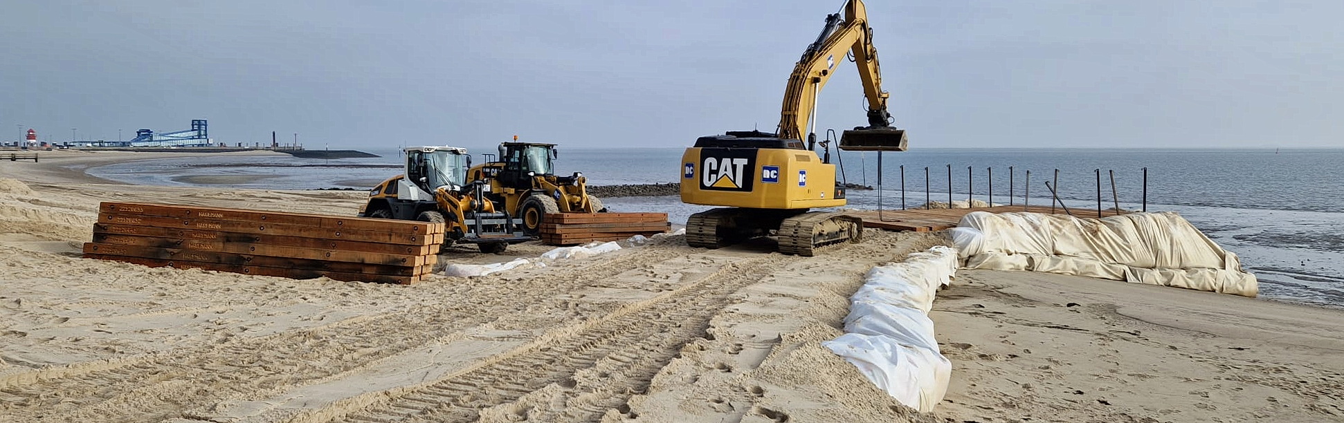 Two wheel loaders and an excavator at work on a construction site on the beach.
